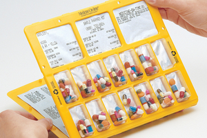 Hands holding a weekly multi-dose medication blister card with printed dosing labels